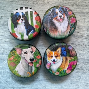 May include: Four round ceramic coasters with colorful images of dogs in a garden setting. The coasters feature a Cavalier King Charles Spaniel, an Australian Shepherd, a Beagle, and a Pembroke Welsh Corgi.