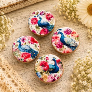 May include: Four circular wooden knobs featuring a printed design of a blue peacock surrounded by vibrant pink, red, and yellow flowers. Each knob has a smooth, rounded surface with a detailed botanical and avian illustration on the front face.
