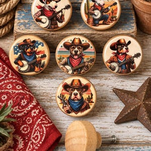 May include: A set of six round wooden cabinet knobs featuring illustrations of dogs dressed as cowboys. The designs include dogs wearing hats and bandanas, playing banjos, or holding a revolver, set against desert or American flag backgrounds.