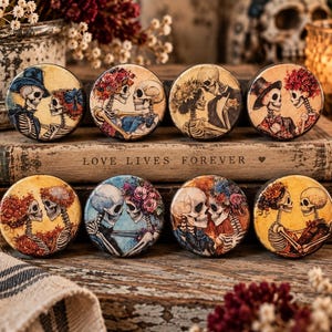 May include: Eight circular decorative buttons featuring illustrations of skeletons in various romantic poses, adorned with colorful floral crowns and hats. Each button displays a unique pair of skeletons, with some wearing formal attire.