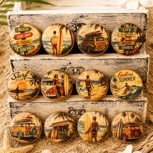 May include: Twelve circular wooden knobs featuring vintage-style surf-themed illustrations. Designs include surfboards, classic woody station wagons, beach signs with text like 'Beach Surf Shop Tacos Good Vibes', and surfers on sandy beaches.