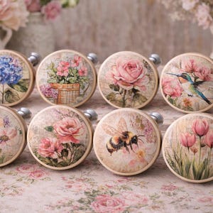 May include: A collection of eight round cabinet knobs with floral and insect designs. Each knob features a different image, including a blue hydrangea, pink roses, a hummingbird, and a bumblebee. The knobs have silver hardware.