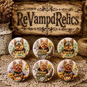 May include: Six round ceramic cabinet knobs featuring illustrations of Yorkshire Terrier dogs surrounded by colorful flowers and Easter eggs. Each knob displays a detailed portrait of a small dog with tan and black fur, set against a white background.