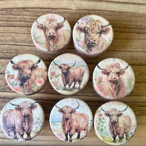 May include: Eight round wooden coasters with a floral design and a highland cow image. The coasters feature a variety of floral patterns and cow poses.