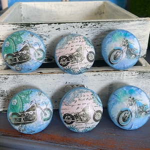 May include: Six blue round decorative drawer pulls with a vintage motorcycle design. Each pull features a different motorcycle design with a blue, white, and black color scheme.