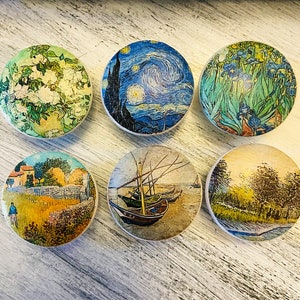 May include: Six round wooden coasters with different painted designs. The coasters feature images of flowers, a starry night sky, a seascape with boats, a landscape with trees, and a landscape with a house.