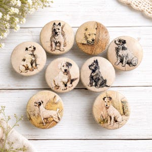 May include: A collection of eight round wooden cabinet knobs, each featuring a different vintage-style illustration of a dog breed. The knobs vary in color, with dogs in shades of brown, black, and white.