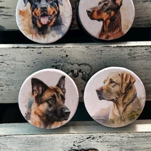 May include: Four round, white, ceramic coasters with watercolor images of different dog breeds. The coasters feature a Rottweiler, a Doberman Pinscher, a German Shepherd, and a Labrador Retriever.