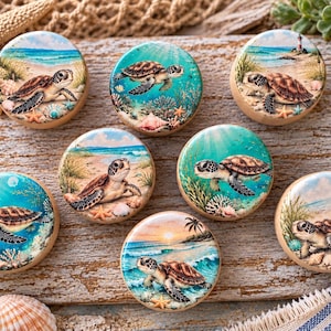 May include: A set of seven round wooden drawer knobs, each featuring a unique, detailed illustration of a sea turtle in a coastal or underwater setting, including sandy beaches, coral reefs, and ocean waves in shades of blue, green, and tan.