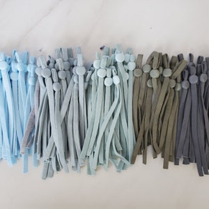 May include: A collection of blue, green, and gray elastic cords with button closures. The cords are arranged in rows and are all the same length.
