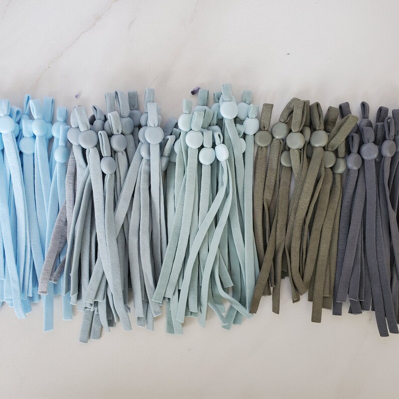 May include: A collection of blue, green, and gray elastic cords with button closures. The cords are arranged in rows and are all the same length.
