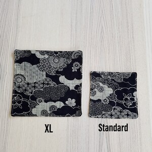 May include: Two black fabric coasters with a white and gray floral pattern. The larger coaster is labeled "XL" and the smaller coaster is labeled "Standard".