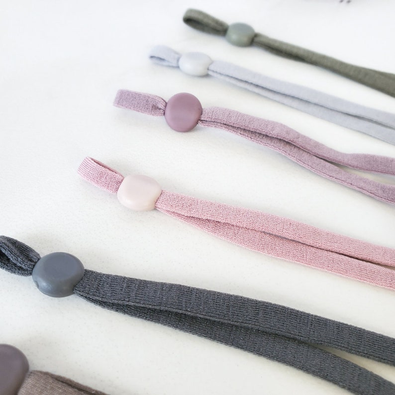May include: Assortment of five different colored elastic cords with adjustable toggles. The cords are in shades of gray, pink, and light purple.