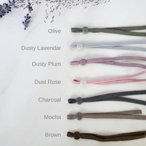 May include: Seven different colors of elastic cord with plastic stoppers. The colors are olive, dusty lavender, dusty plum, dust rose, charcoal, mocha, and brown.