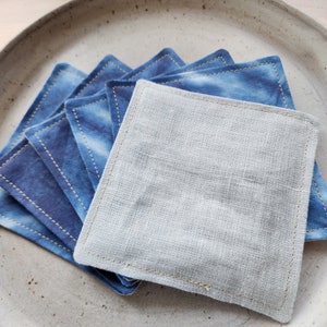 May include: A stack of blue and white fabric squares with a stitched edge. The top square is white and the rest are blue with a tie-dye pattern.