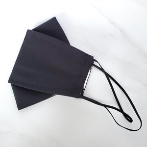 以下が含まれることがあります： 調節可能なストラップが付いた濃いグレーのフェイスマスク。マスクは柔らかく通気性の良い生地で作られています。