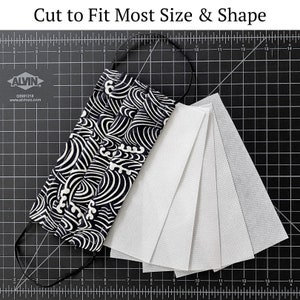 May include: A black and white patterned fabric face mask with a black elastic band. The mask is laid out on a black cutting mat with five white filter inserts.