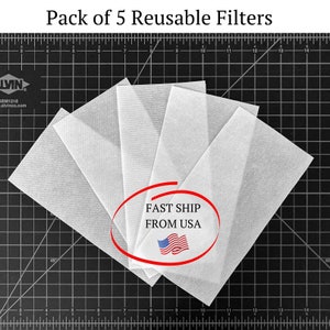 May include: Pack of 5 white reusable filters for a face mask. The filters are laid out on a black cutting mat with a ruler. The text "FAST SHIP FROM USA" is in a red circle with a small American flag.