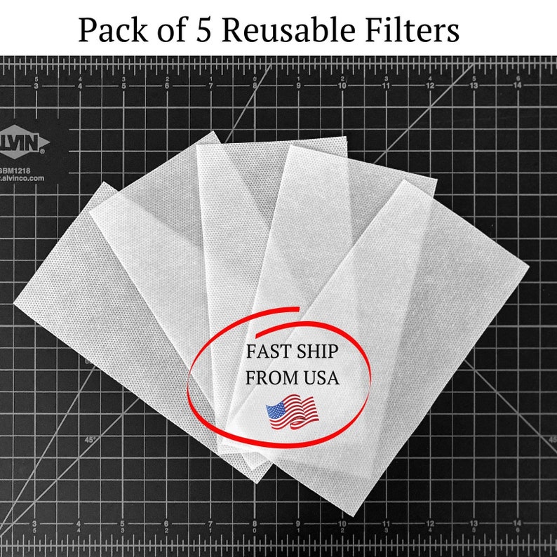 May include: Pack of 5 white reusable filters for a face mask. The filters are laid out on a black cutting mat with a ruler. The text "FAST SHIP FROM USA" is in a red circle with a small American flag.