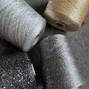 May include: Four spools of decorative yarn in silver, gold, and black. The yarn is wound around cardboard cores. The silver yarn has a metallic sheen, while the black yarn is embellished with sequins. The gold yarn has a warm, shimmering appearance.