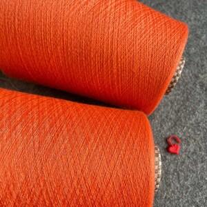 May include: Two spools of bright orange yarn. The yarn is wound tightly on the spools and has a smooth, even texture.