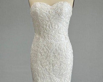 May include: A white strapless wedding dress with a fitted bodice and a flowing skirt. The dress is covered in delicate floral lace and beading.