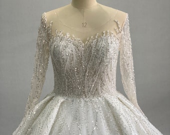 Puede incluir: Un vestido de novia blanco con mangas largas y una falda completa. El vestido está cubierto de lentejuelas y cuentas.