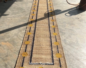 May include: A long, rectangular jute runner rug with a natural tan color. The rug features a border with dark blue lines and yellow circular accents. The text "Majestic Rugs Decor" is visible on the rug.