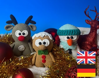 Puede incluir: Tres adornos navideños de crochet: un reno, un hombre de jengibre y un muñeco de nieve. Los adornos están rodeados de oropel dorado y adornos rojos. La imagen también incluye una figura de reno roja y dorada y una bandera del Reino Unido y Alemania.