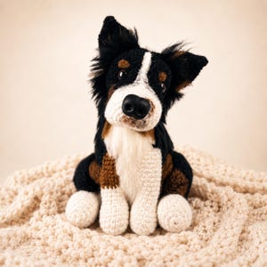 Può includere: Una statuetta di cane realizzata all'uncinetto a mano con un mantello tricolore in filato nero, bianco e marrone. Il peluche presenta orecchie a punta, un naso nero prominente e occhi scuri, con petto e zampe di colore bianco.