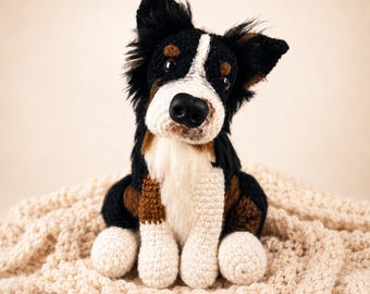 Puede incluir: Una figura de perro tejida a ganchillo a mano con un pelaje tricolor de hilo negro, blanco y marrón. El juguete de peluche tiene orejas puntiagudas, una nariz negra prominente y ojos oscuros, con el pecho y las patas de color blanco.