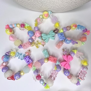 May include: A set of six colorful bracelets with various charms, including hearts, bows, stars, and the word "LOVE". The bracelets are made of plastic beads and are perfect for adding a touch of whimsy to any outfit.