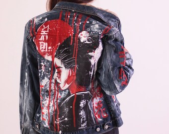Könnte beinhalten: Jeansjacke mit einem bemalten Design auf der Rückseite. Das Kunstwerk zeigt eine rote Sonne, ein Frauenprofil und japanische Schriftzeichen. Weiße Farbspritzer und rote Tropfen verstärken den künstlerischen Effekt. Die Jacke ist blau.
