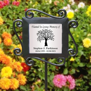 May include: Black metal garden stake with a white ceramic plaque that reads "Planted In Loving Memory of Stephen J. Parkinson 08/06/1999-02/08/2021". The plaque features a black silhouette of a tree.