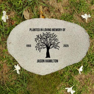 May include: A gray stone memorial with a black tree silhouette and the text "Planted in loving memory of Jason Hamilton 1955 - 2025".