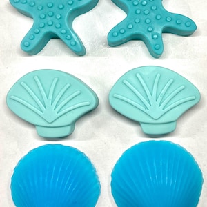 May include: A selection of sea-themed soaps in shades of blue. The collection includes two starfish, two fan-shaped shells, and two scallop shells. The soaps are a solid colour and have detailed textures.