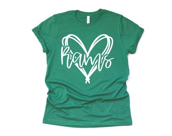 Peut inclure: T-shirt vert avec des manches retroussées. Le t-shirt présente un motif en forme de cœur blanc avec le mot "Rams" écrit à l'intérieur en cursive. Le t-shirt est en matière souple.