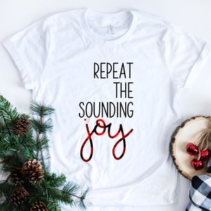 May include: White t-shirt with the text "REPEAT THE SOUNDING joy" in black and red plaid lettering.