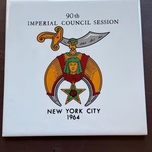 Pode incluir: Azulejo quadrado branco com um emblema colorido. O emblema apresenta um sabre dourado, um design vermelho e dourado e uma estrela com uma rosa. O texto diz "90th IMPERIAL COUNCIL SESSION NEW YORK CITY 1964".