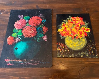 May include: Two floral paintings on black backgrounds. One features red flowers in a teal vase, the other has yellow and orange flowers in a yellow vase. Both paintings have a dark, textured appearance.