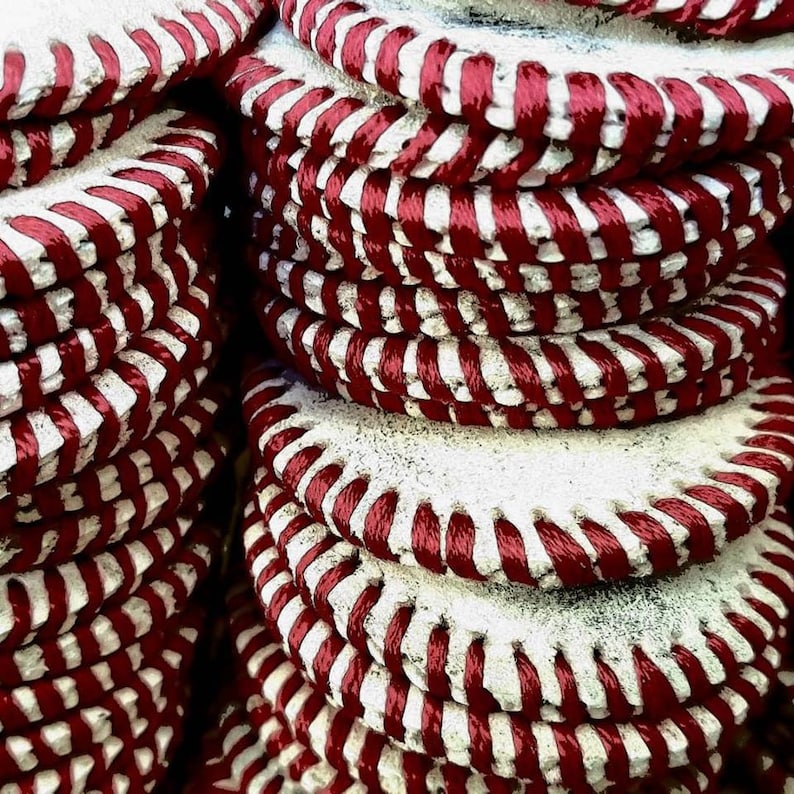 Peut inclure: Une pile de balles de baseball en cuir blanc avec des coutures rouges. Les balles de baseball sont empil&eacute;es les unes sur les autres, cr&eacute;ant un motif rouge et blanc.