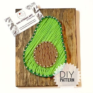 Könnte beinhalten: DIY String Art Muster einer Avocado auf einem Holzgrund. Die Avocado ist aus grünem und braunem Garn gefertigt und hat einen grünen und silbernen Rand.