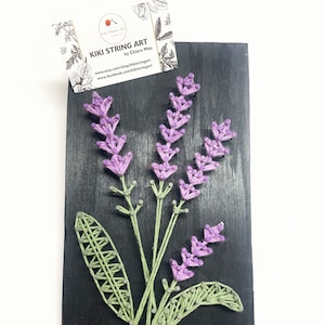 May include: Purple and green string art of lavender flowers on a black wooden background. The art is titled "Kiki String Art" by Chiara Mau.
