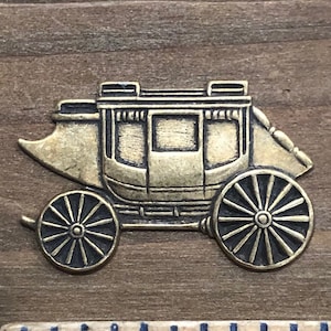 May include: A gold-colored metal charm in the shape of a stagecoach. The stagecoach has a detailed design with wheels, a roof, and a passenger compartment. The charm is about 1 inch in length.