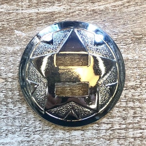 May include: A silver metal star-shaped concho with a decorative design. The concho has two rectangular cutouts in the center.