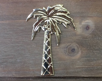 May include: A gold-colored metal palm tree cutout. The palm tree has a detailed trunk and leaves.