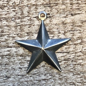 May include: A silver five-pointed star charm with a loop at the top. The star is a rustic, distressed silver color.