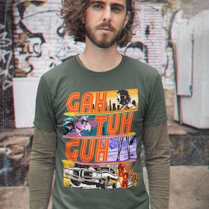 May include: A green t-shirt with a retro-style graphic print featuring a car, a cityscape, and the words "GAH TUH GUH".