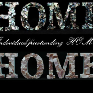 Op de afbeelding: Twee sets van vrijstaande "HOME"-letters, waarbij elke letter is gemaakt van individuele stukjes iriserende schelp. De bovenste set is in tinten blauw en groen, terwijl de onderste set in tinten wit en roze is.