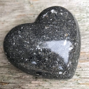 Może przedstawiać: Czarny kamień w kształcie serca z białymi plamkami. Kamień jest wypolerowany i gładki.